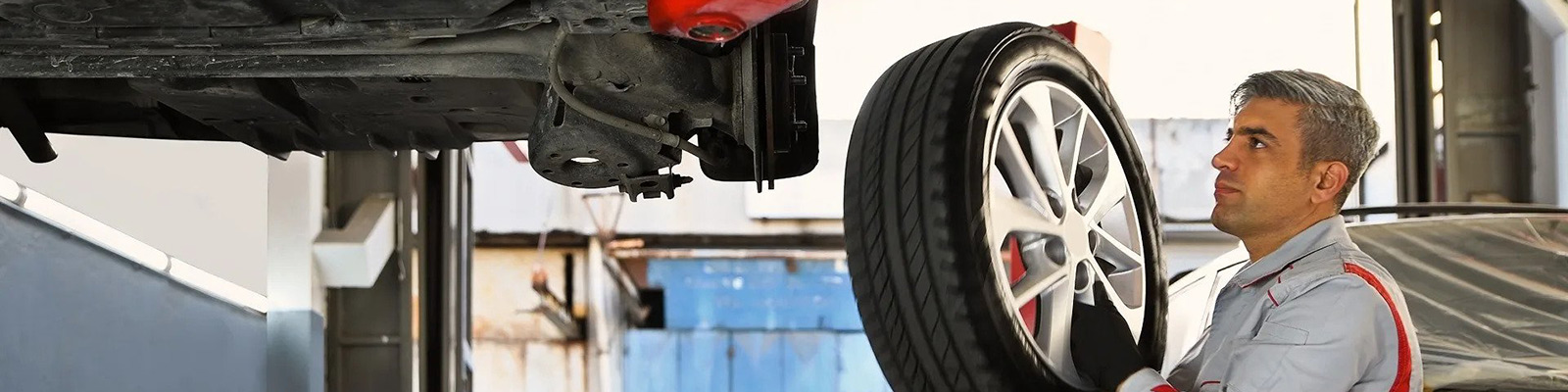 man standing under raised car holding a wheel